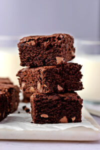 A Stack of Brownies on a Parchment Paper Served with Milk in the Background