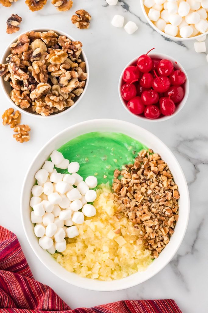 Pineapple minced, chopped walnuts, marshmallows and jello in a white bowl.