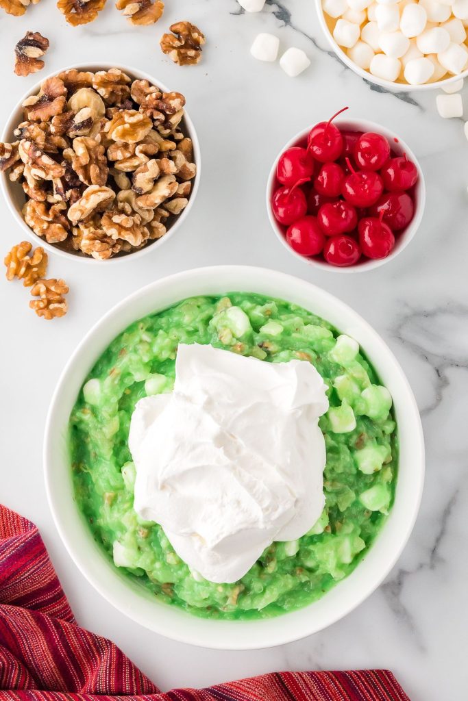 Whipped cream added on top of marshmallow and jello mixture in a white bowl.