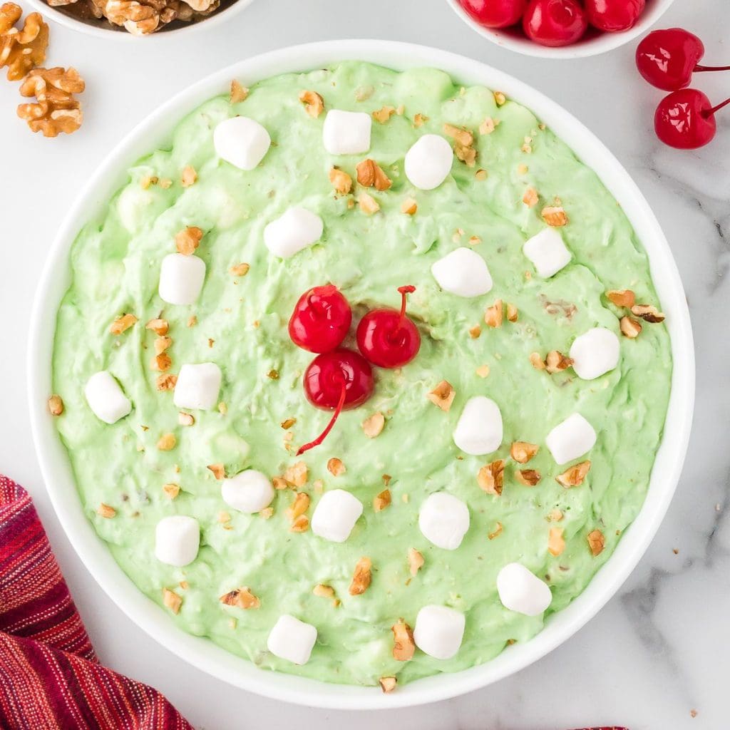 Watergate salad in a white bowl with cherries, marshmallows and chopped walnuts on top.