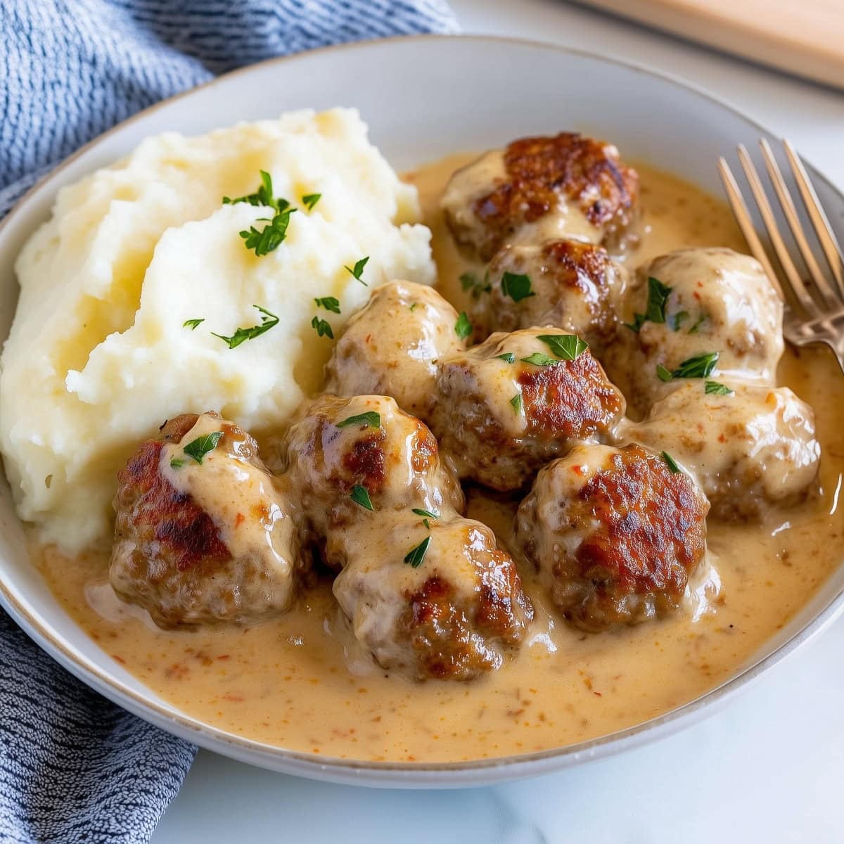 Ikea meatballs with gravy and mashed potatoes with fork on the side on a white plate.
