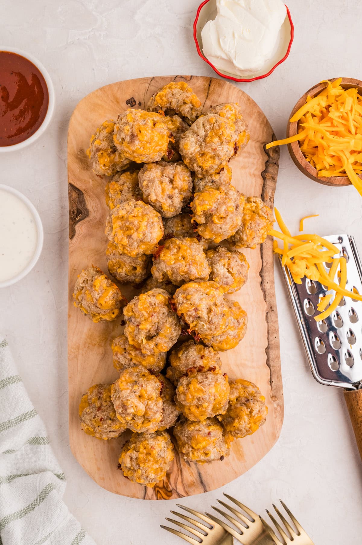 Bisquick sausage cheese balls on a wooden cutting board. Shredded cheese and dipping sauce on the side.