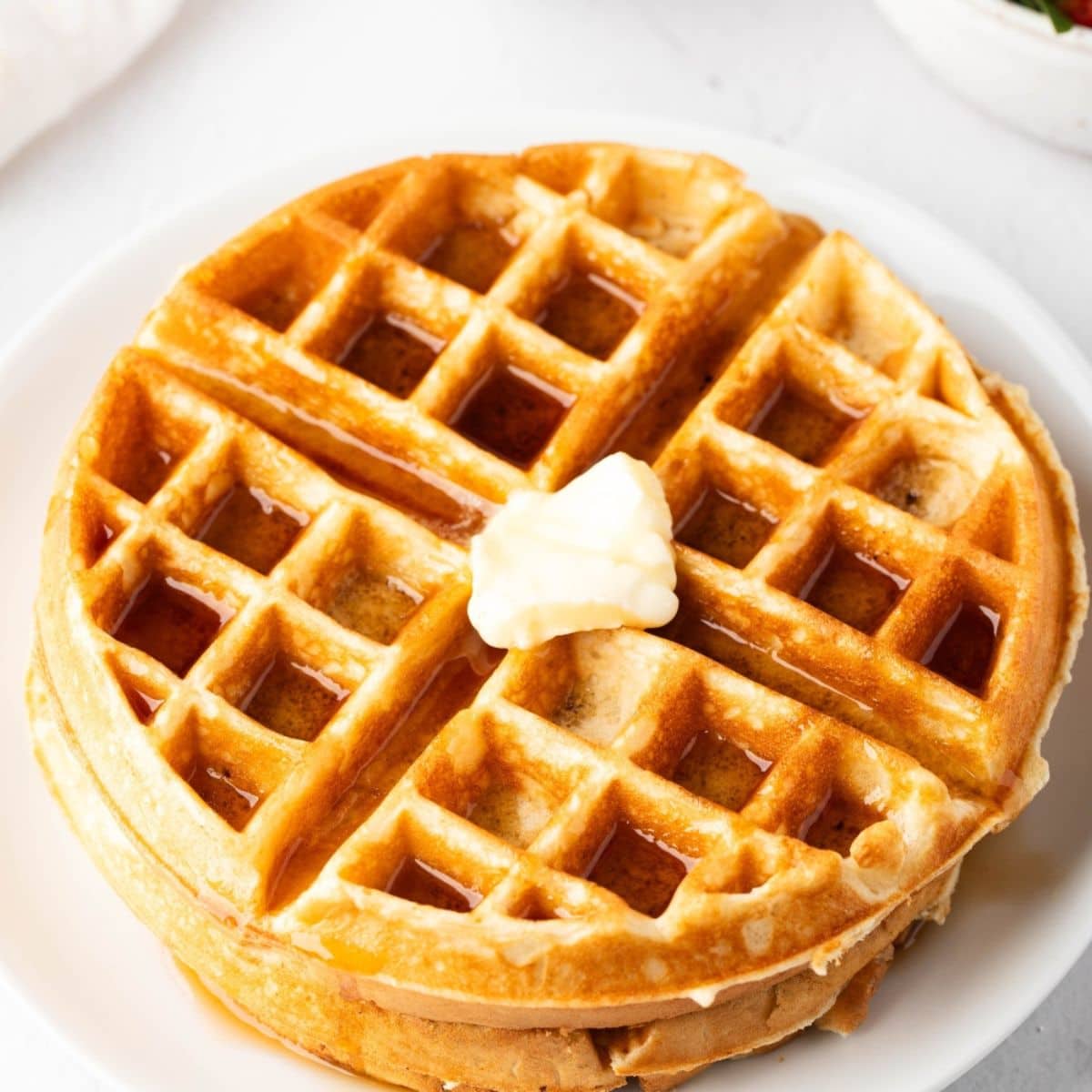 Stack of waffle with a slice of butter on top served in a white plate.