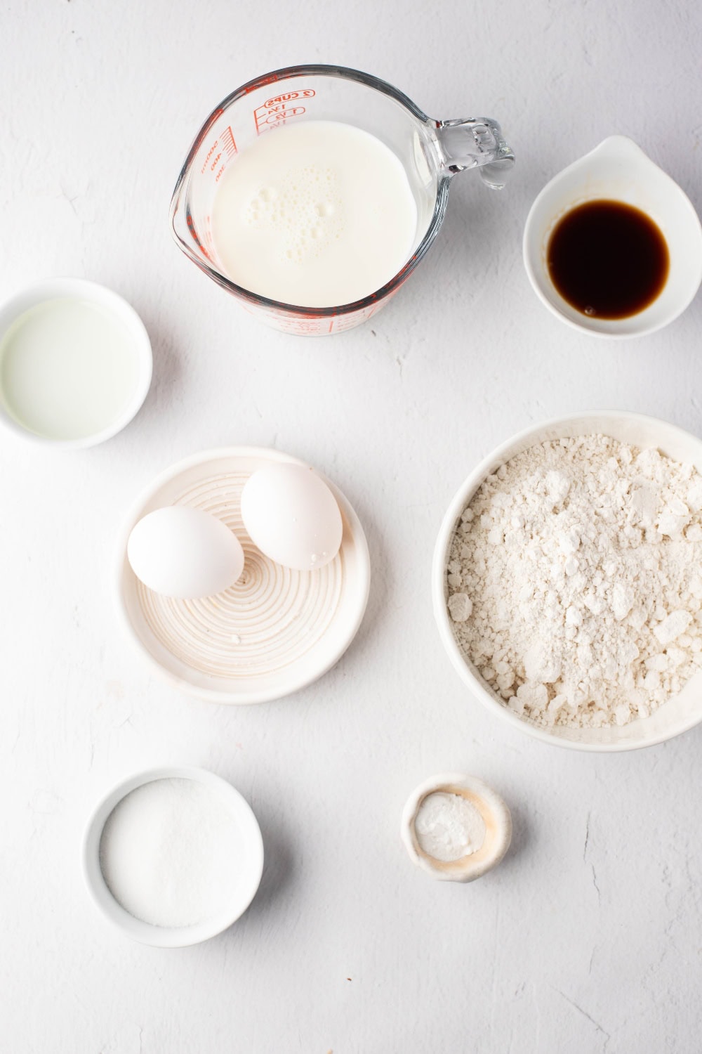 Eggs, waffle mix, milk, vanilla sitting on a concrete table.