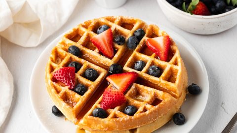Waffles served in a white plate garnished with sliced strawberries and bluberries.
