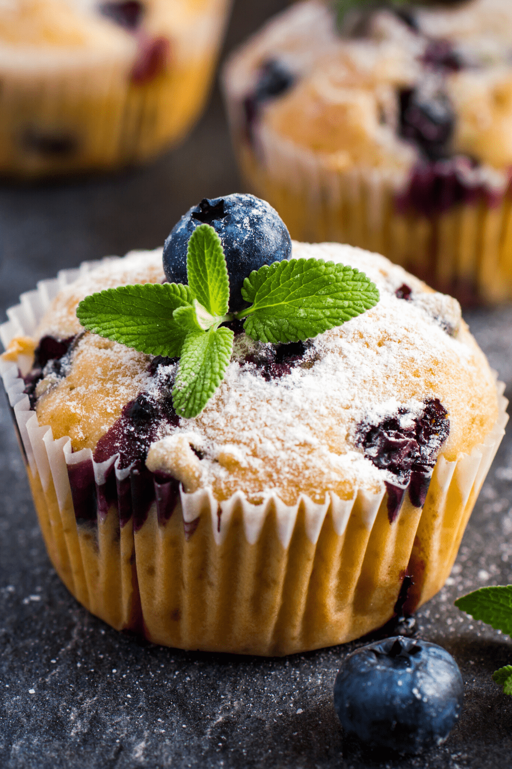 Muffins with speckles of blueberries dusted with powdered sugar. 