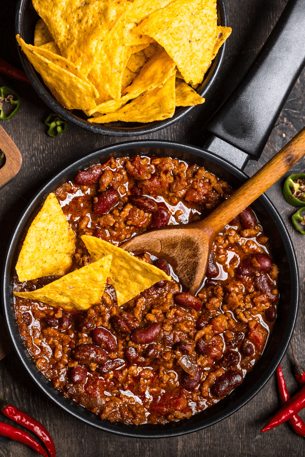 Chili with red beans and tortilla chips on  a black bowl. 