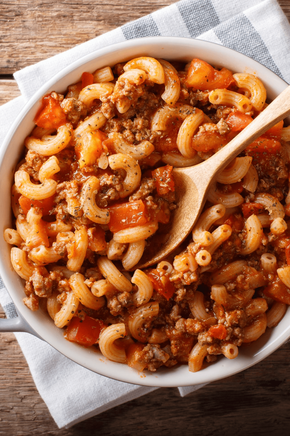 Bowl of macaroni pasta in tomato sauce and ground beef served on a bowl with wooden spoon