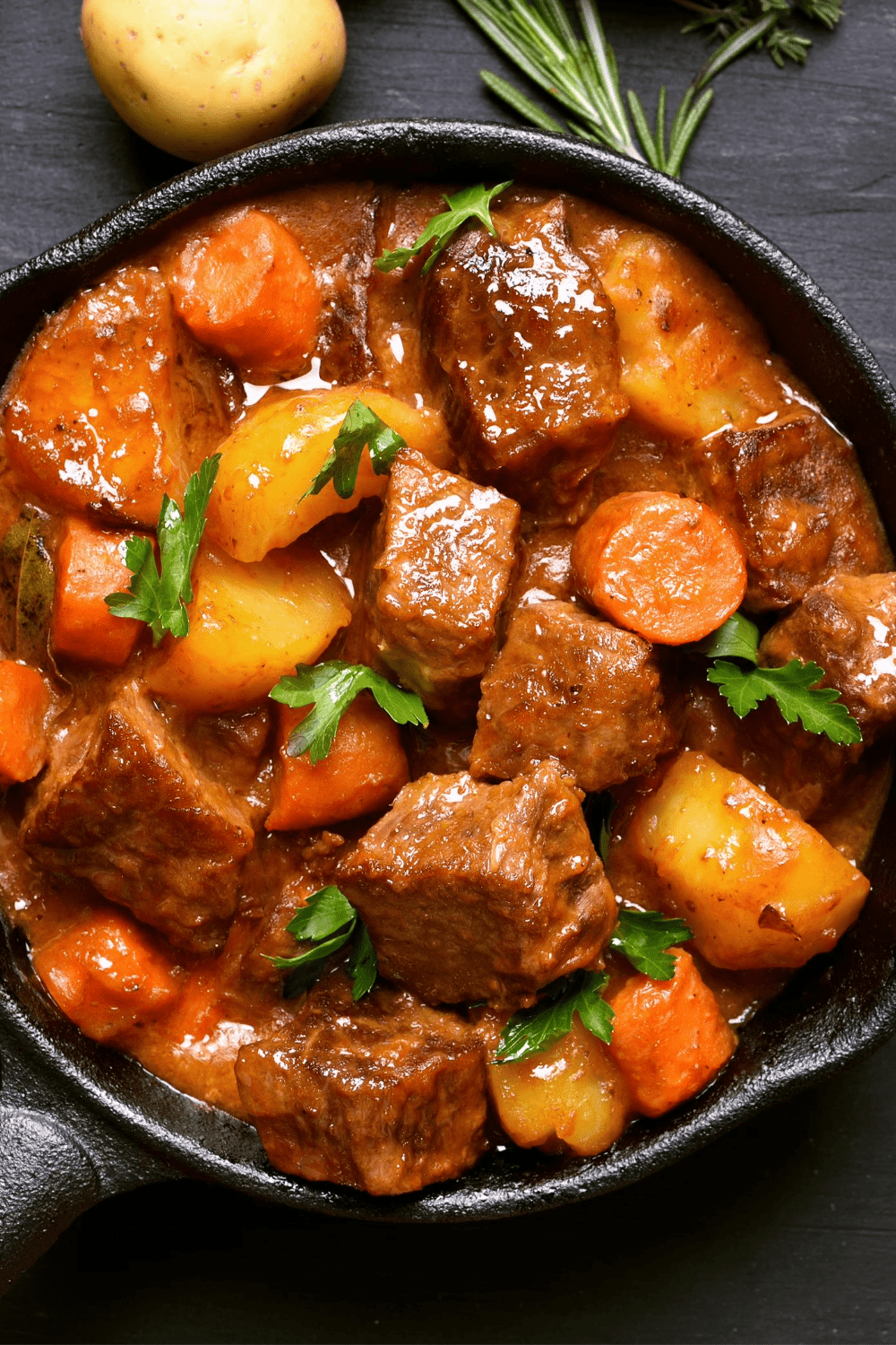 Beef Stew with carrots and potatoes on cast iron, garnished with cilantro leaves