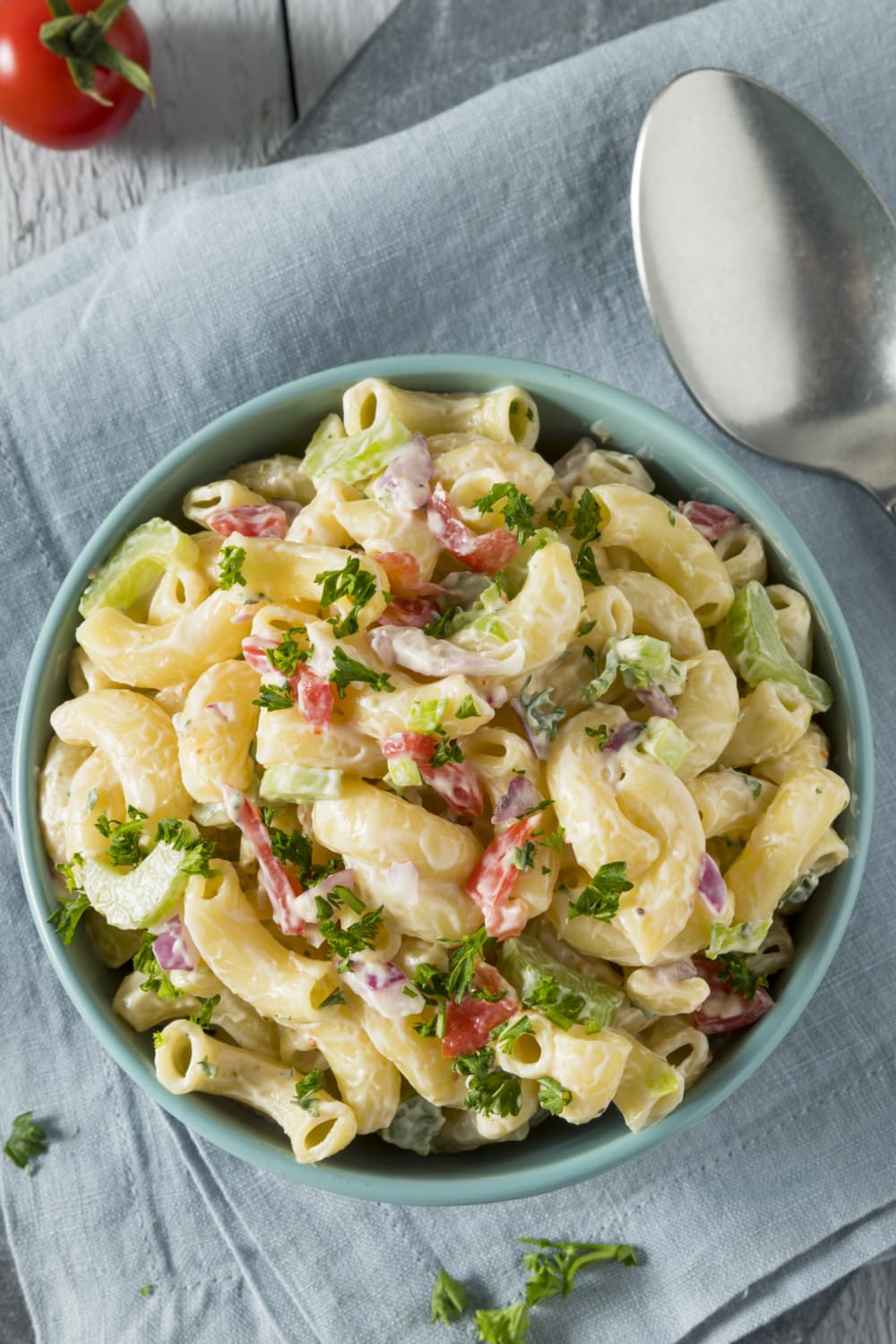 Bowl of elbow pasta with mayonnaise, chopped celery, onions, red and green bell peppers and garnished with parsley