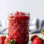 Strawberry Glaze in a Glass Jar on a White Marble Table with Fresh Strawberries Around the Jar