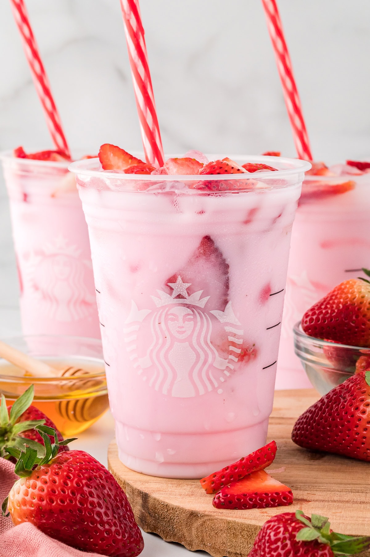 Three clear Starbucks cups filled with Starbucks Pink Drink, topped with fresh strawberries, side view