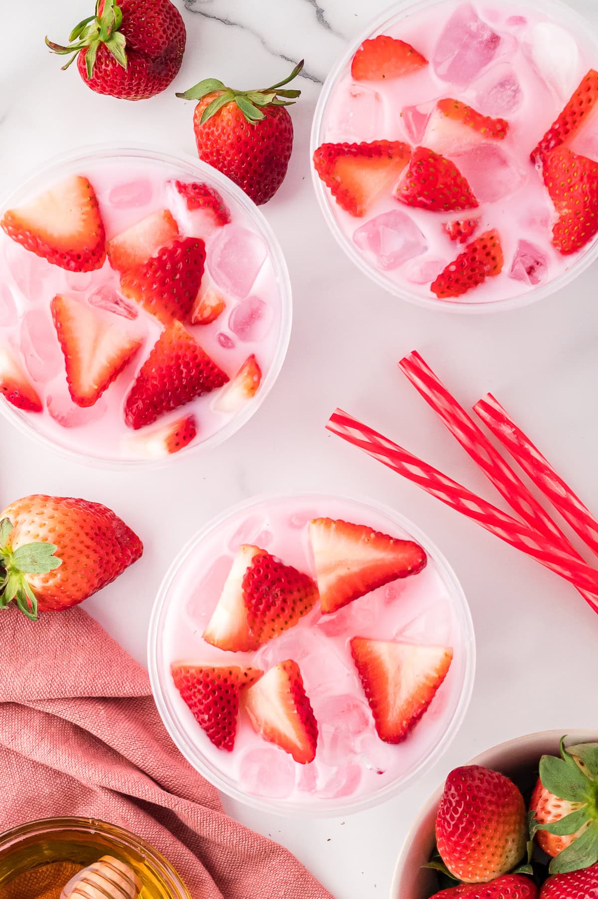 Three Starbucks Pink Drinks in clear Starbucks cups, garnished with fresh strawberries, top view