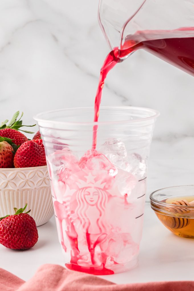 TAZO passion tea poured from a glass pitcher into a Starbucks cup half filled with ice.