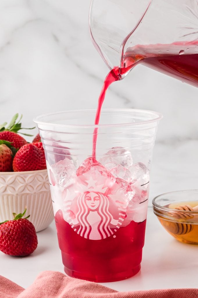 TAZO passion tea poured from a glass pitcher into a Starbucks cup half filled with ice.