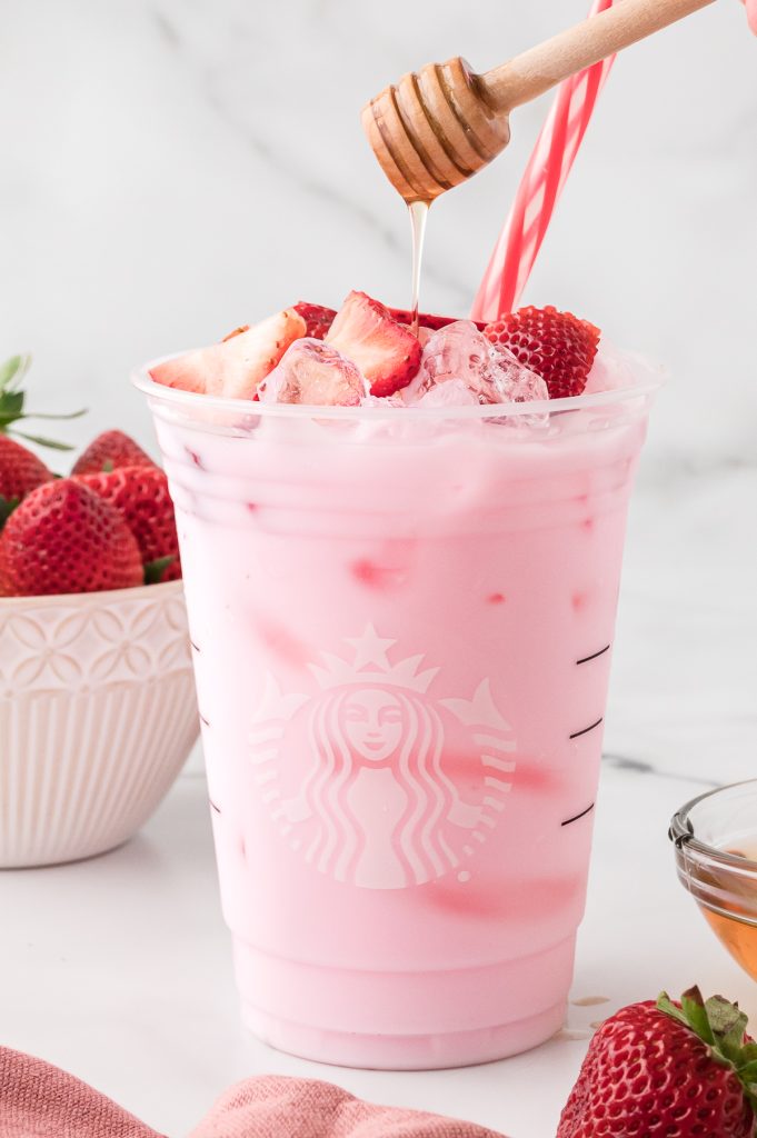 Starbucks Pink Drink in a Starbucks cup, garnished with fresh strawberries and agave syrup drizzled on top