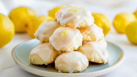 Pile of Lemon Drop Cookies with Lemon Icing on a Plate with Fresh Lemons in the Background