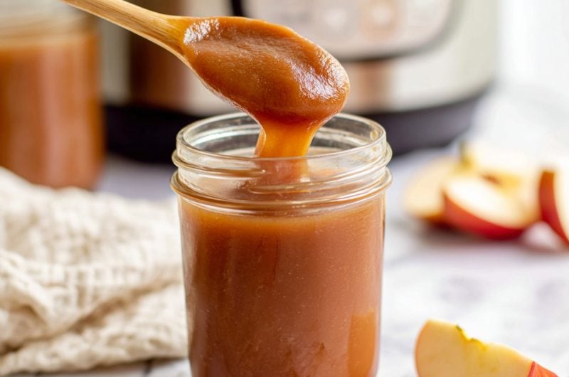 Homemade slow cooker apple butter in a glass jar with a wooden spoon dripping back to the jar.
