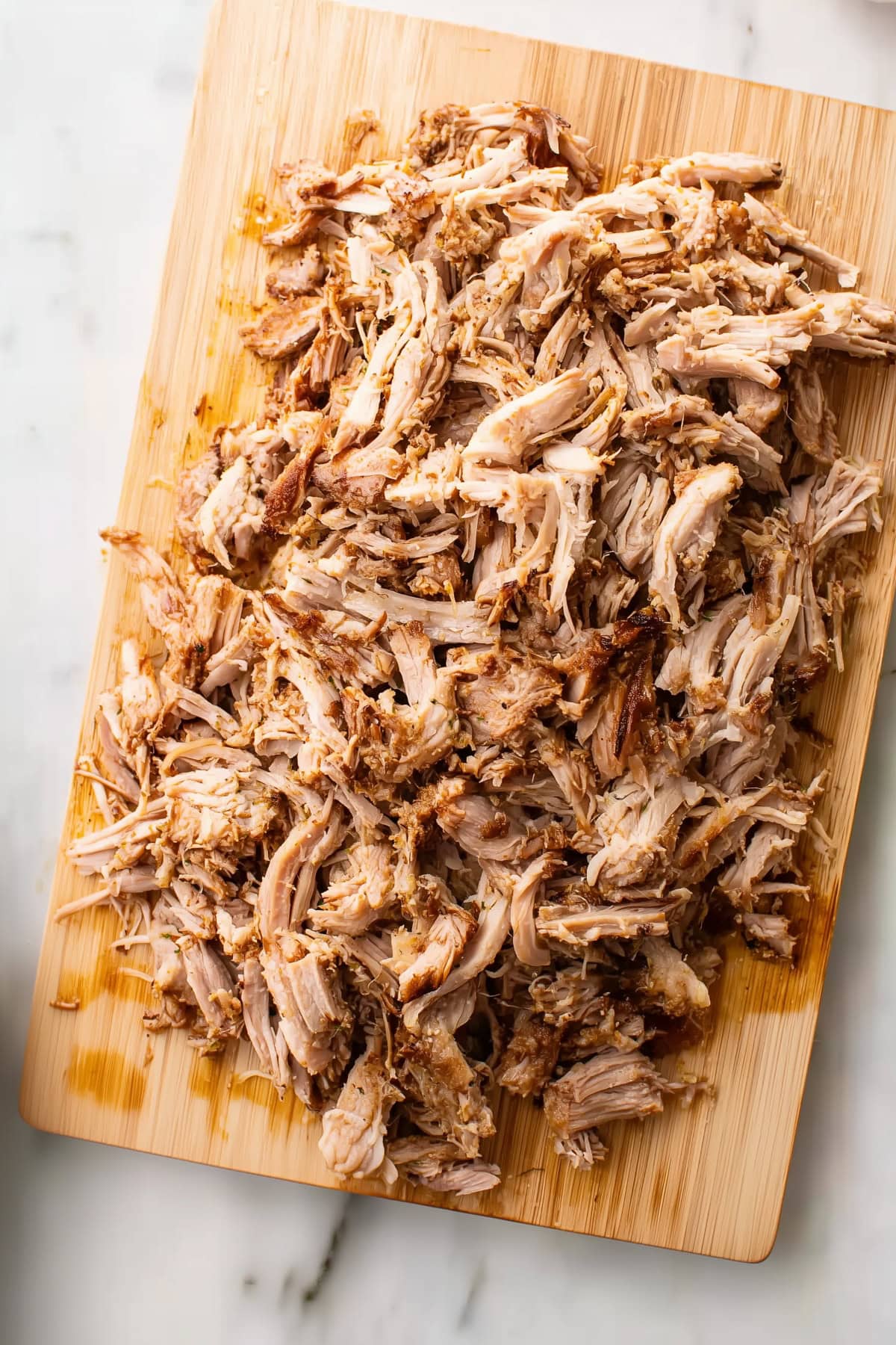 Shredded pulled pork piled on a wooden cutting board.
