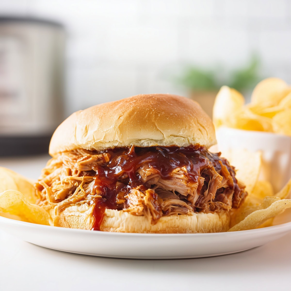 Pulled pork sandwich with chips on a white plate.