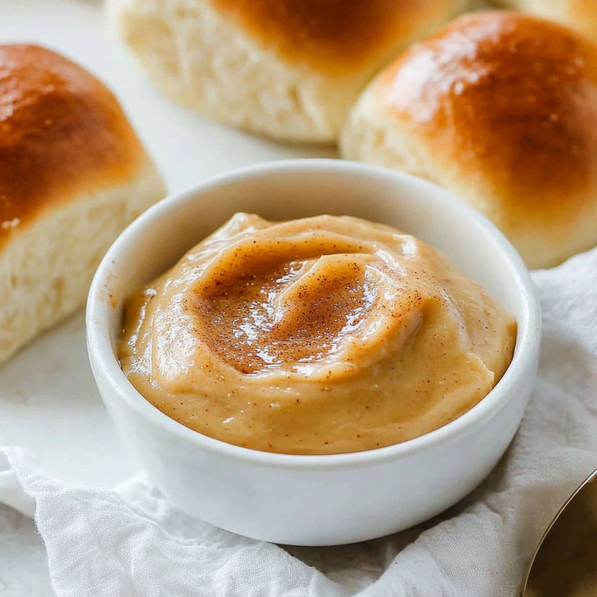 Texas Roadhouse cinnamon honey butter in a small white bowl with dinner rolls on the side