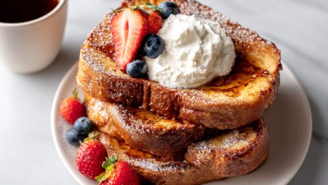 Baileys french toast with whipping cream and berries in a plate, served with a cup of coffee.