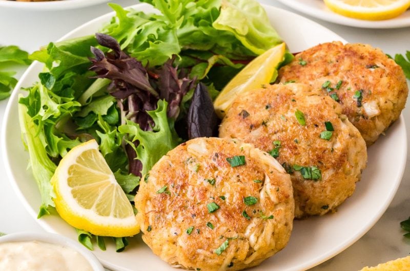 Crab cake patties served with fresh vegetables and lemon wedges in a plate.