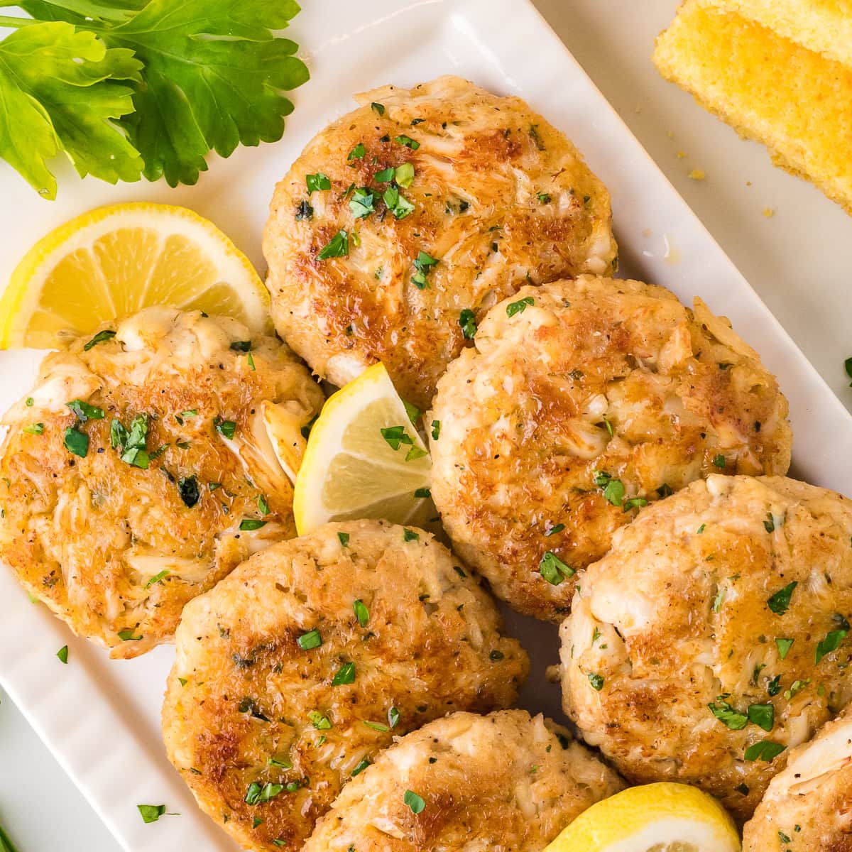 Crab cakes with parsley and lemon wedges, on a white plate