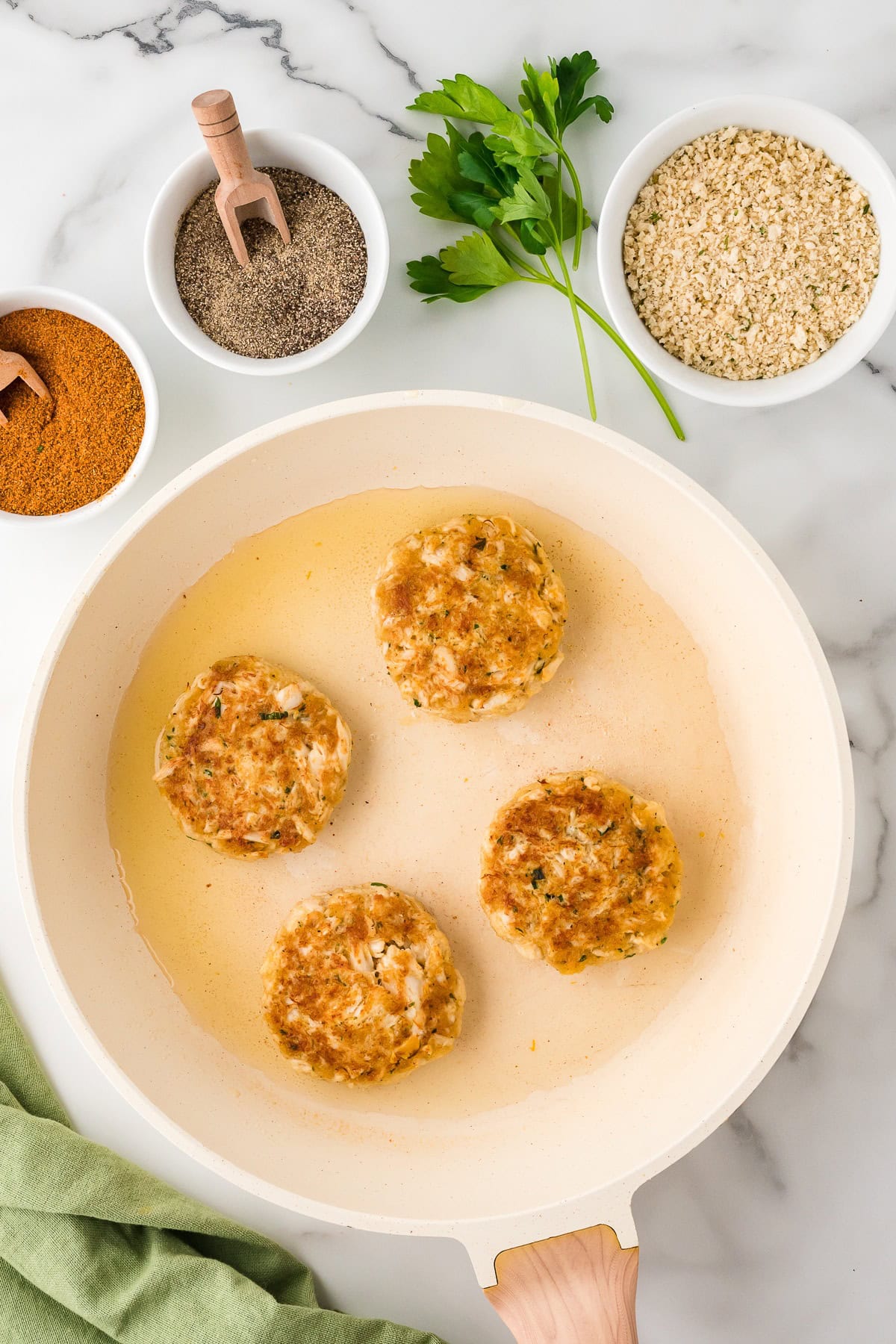 Fried crab cake patties in a skillet with ingredients on the side, top view