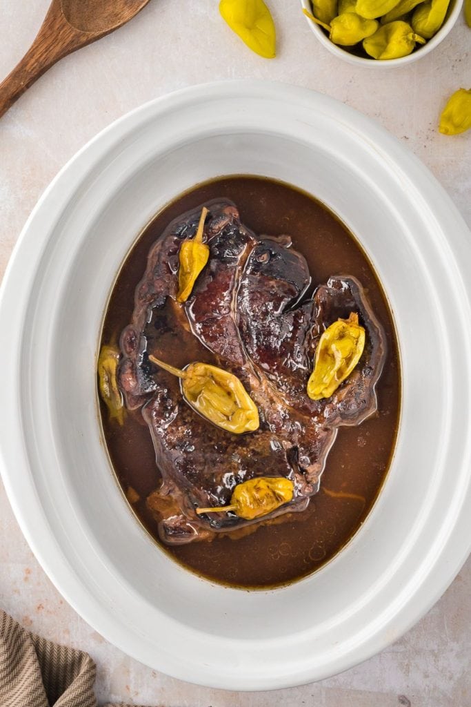 Cooked Mississippi Pot Roast inside a slow cooker with gravy and pepperoncini peppers, top view