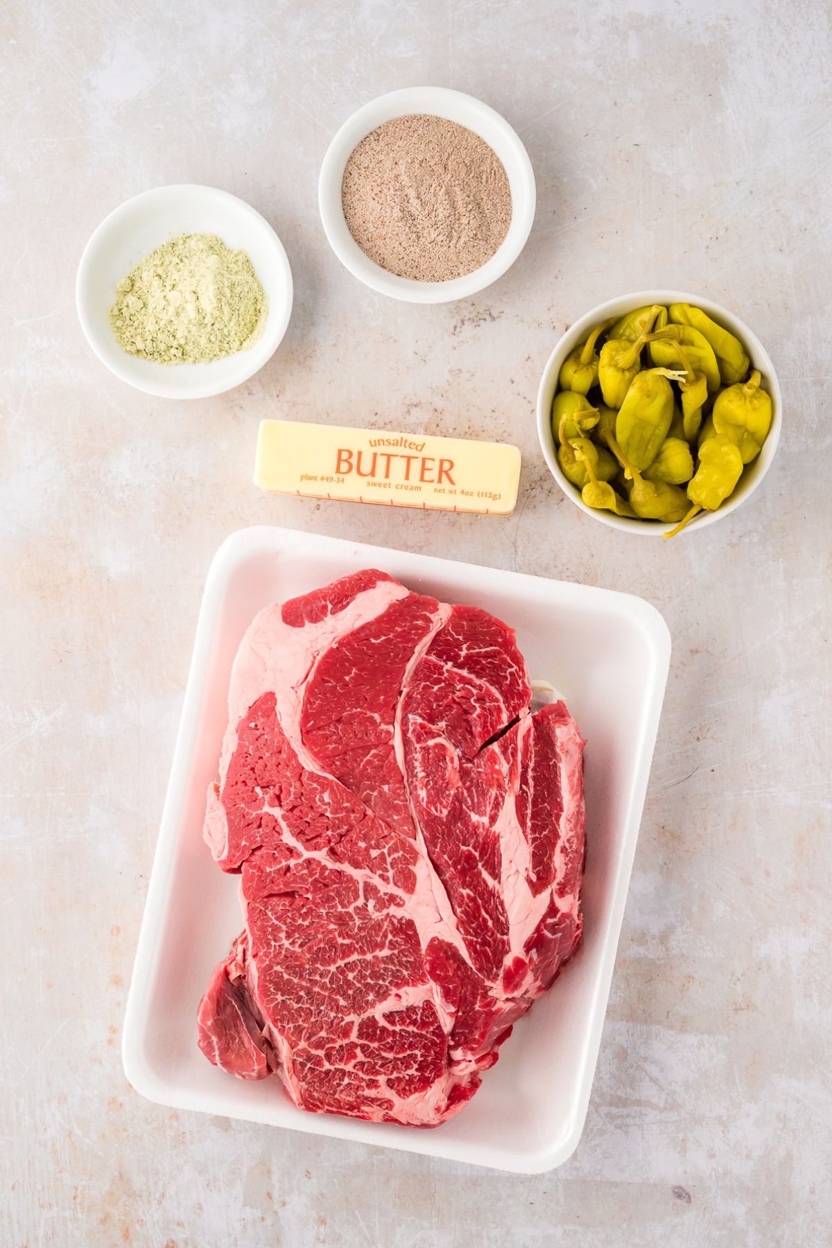 Pot Roast Ingredients Photo: Whole chuck roast, pepperoncini pepper, peppers. gravy mix, dry ranch seasoning, and a stick of butter, top view