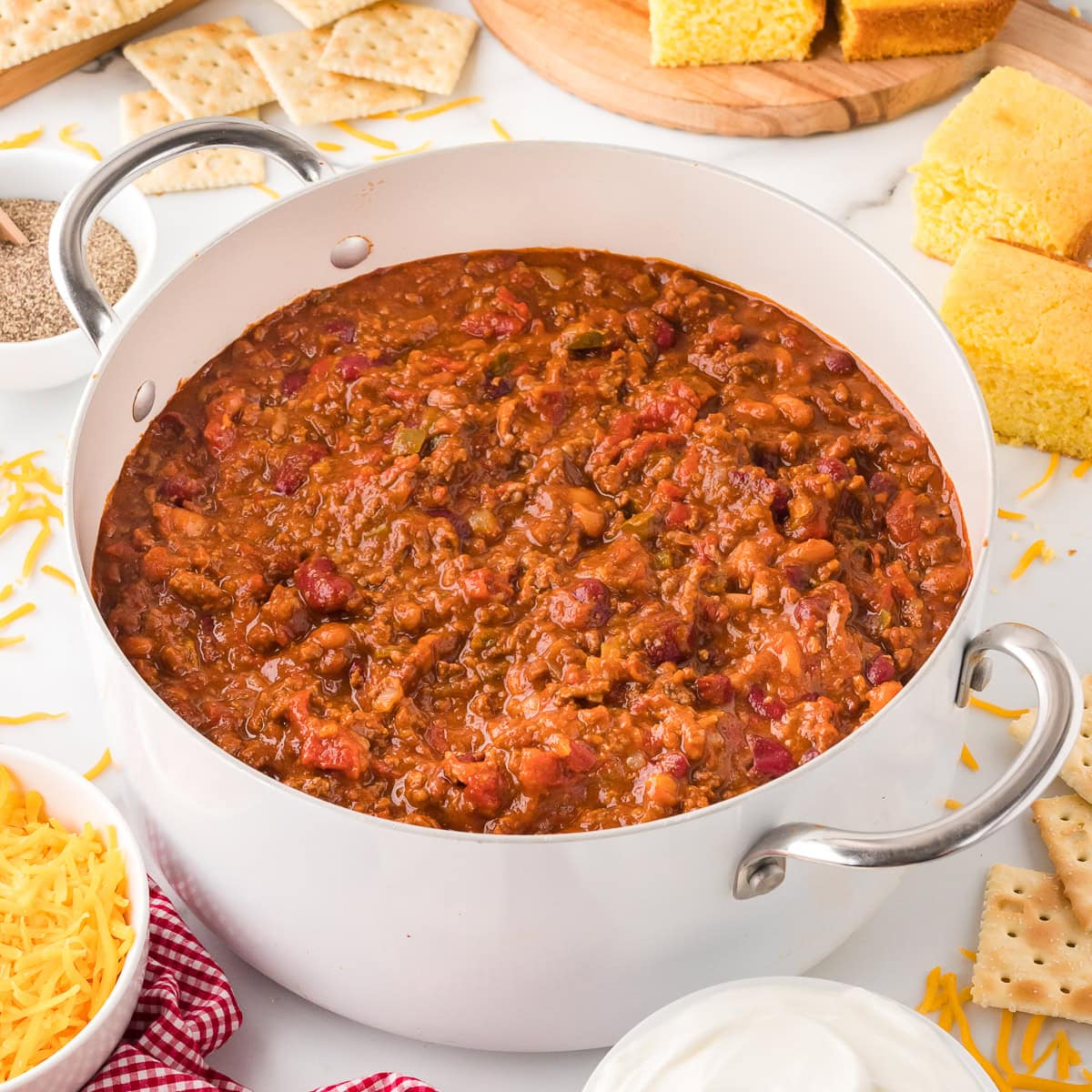 Wendy's Chili with ground beef, beans and bell peppers in a large pot with cheese, cornbread, and crackers on the side