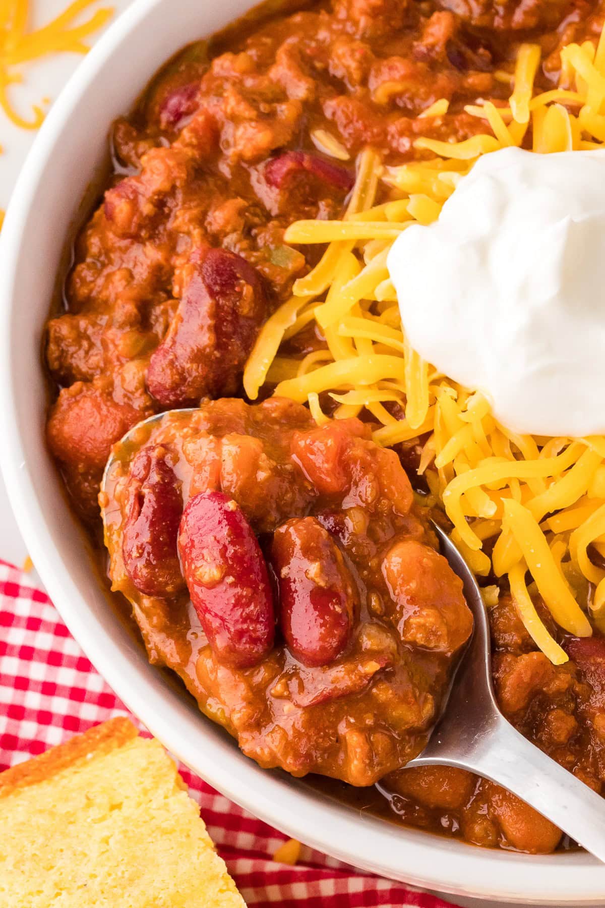 A bowl of bean and beef chili topped with sour cream and shredded cheese in a bowl, close up