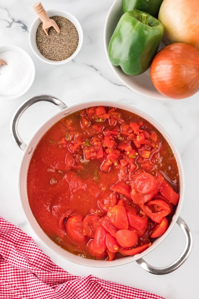 Stewed tomatoes in a large pot with vegetables on the side, top view