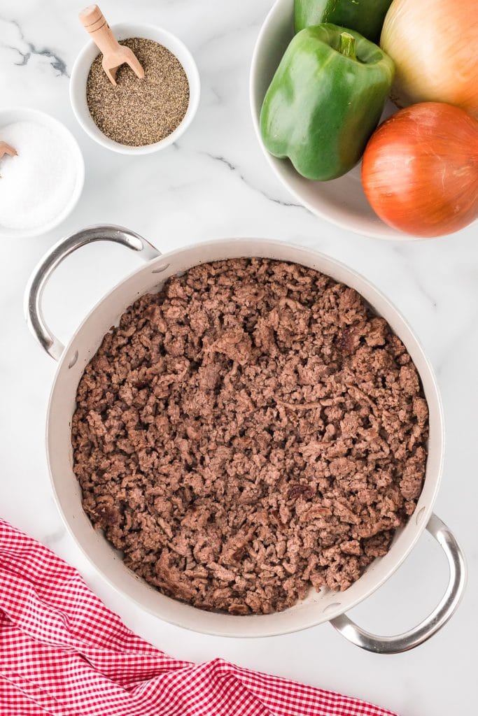 Cooked ground beef in a large pot with vegetables, salt and pepper on the side, top view