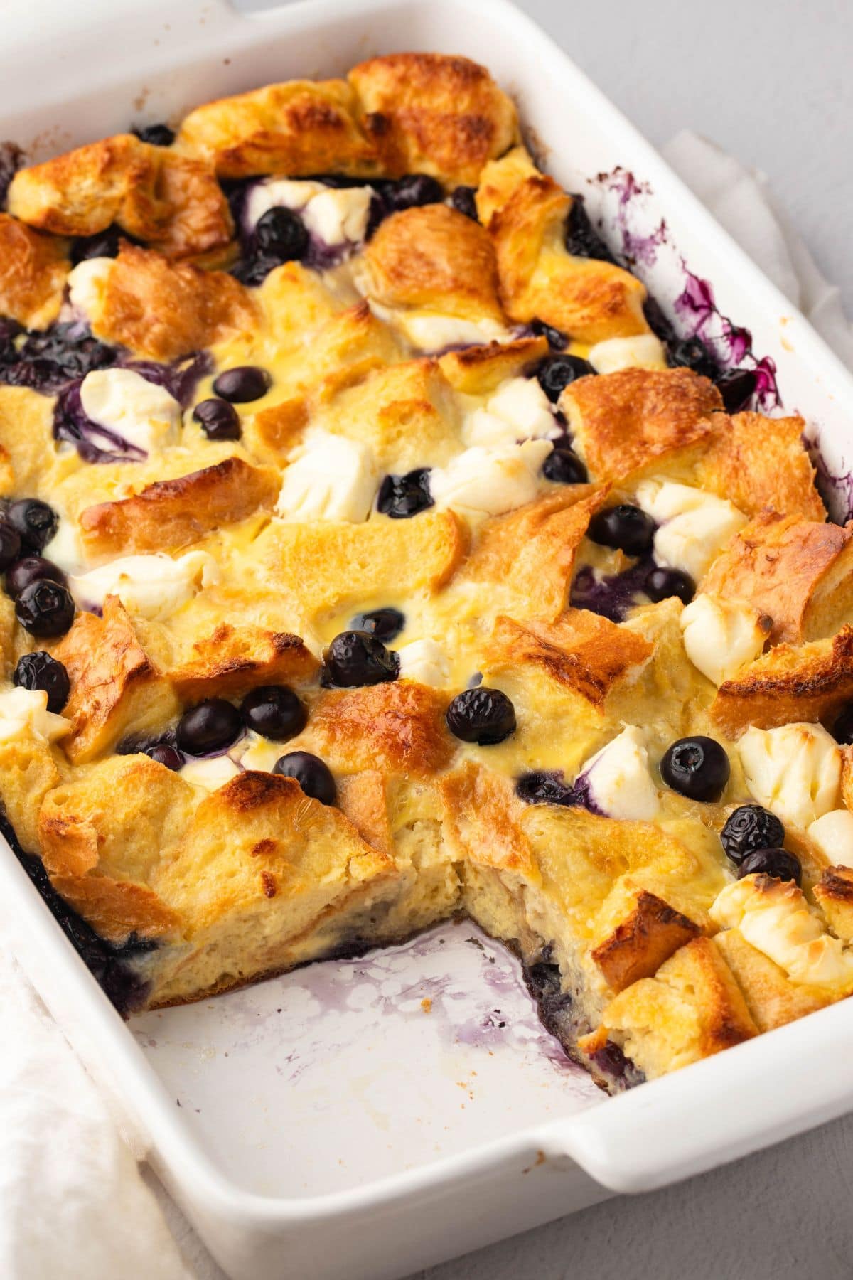 Blueberry French toast casserole slice missing in a rectangular white baking dish.
