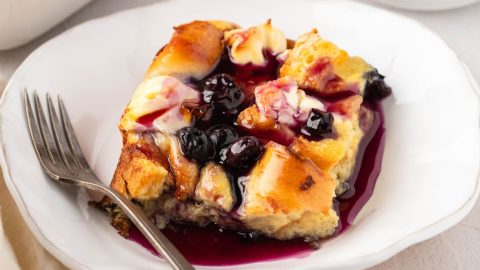 Slice of blueberry French toast casserole with jam on top served on a white plate.