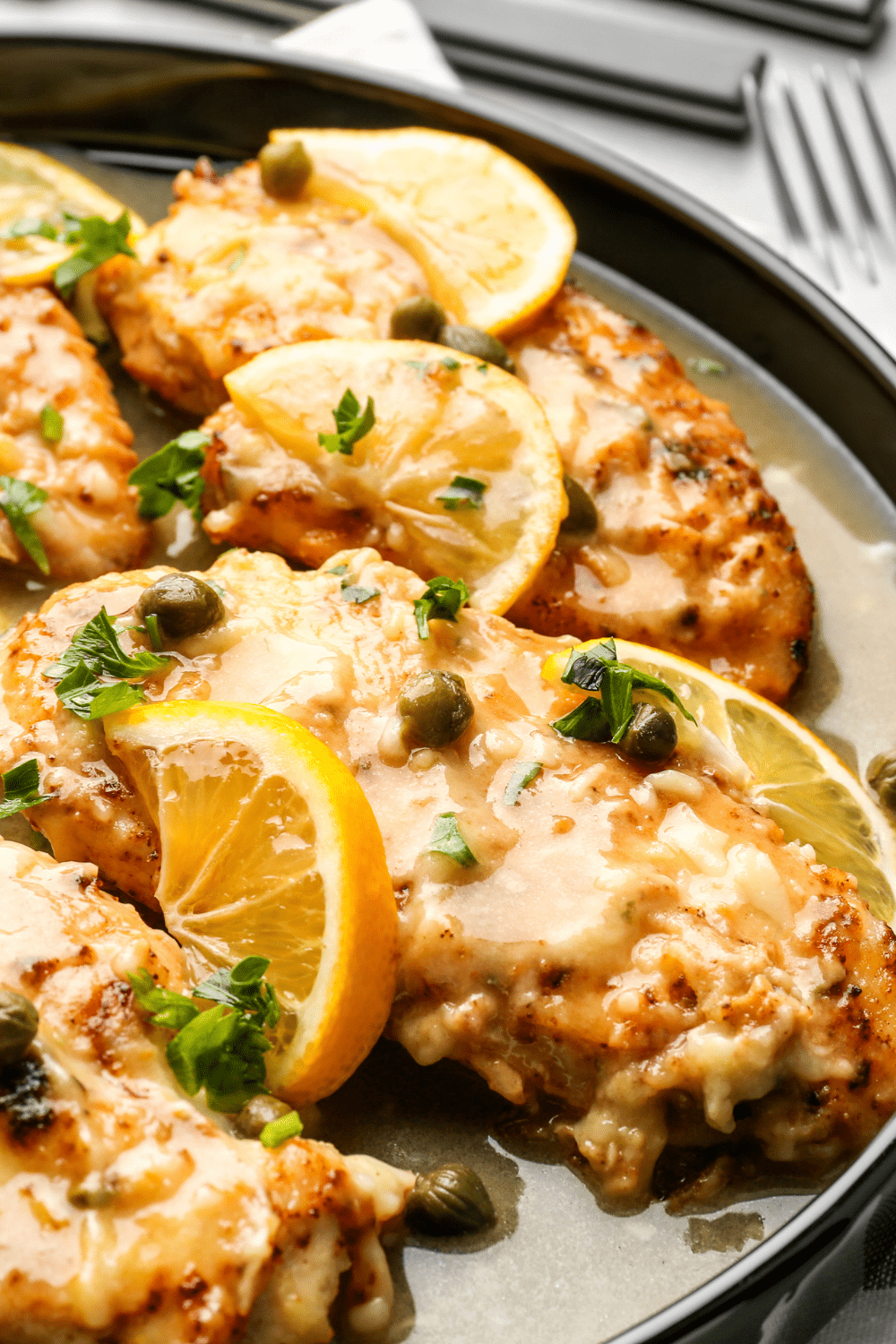Chicken piccata in a pan with sauce and lemon slices.