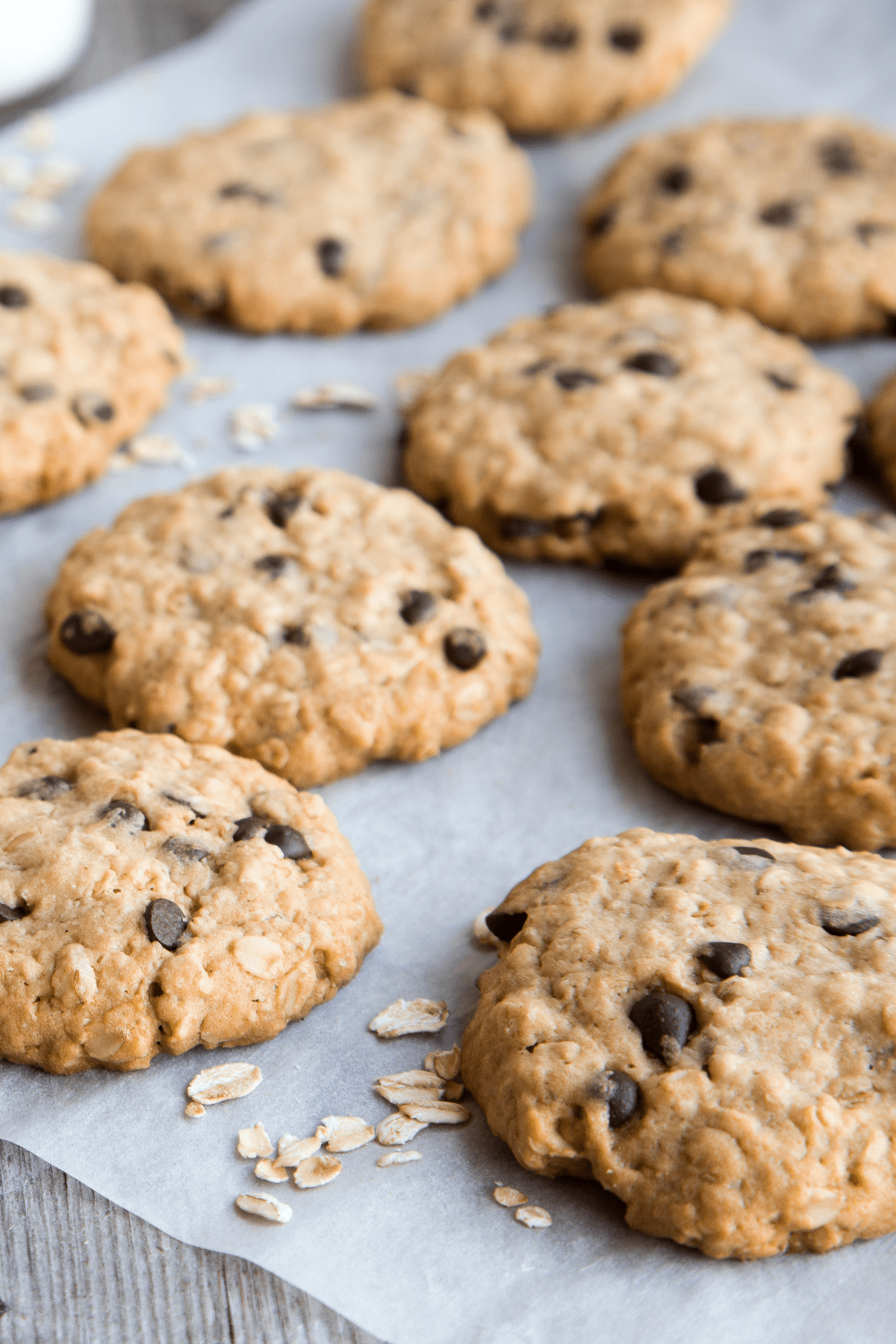 Fresh baked cookies with chocolate chips arranged in a sheet pan layered with parchment paper. 