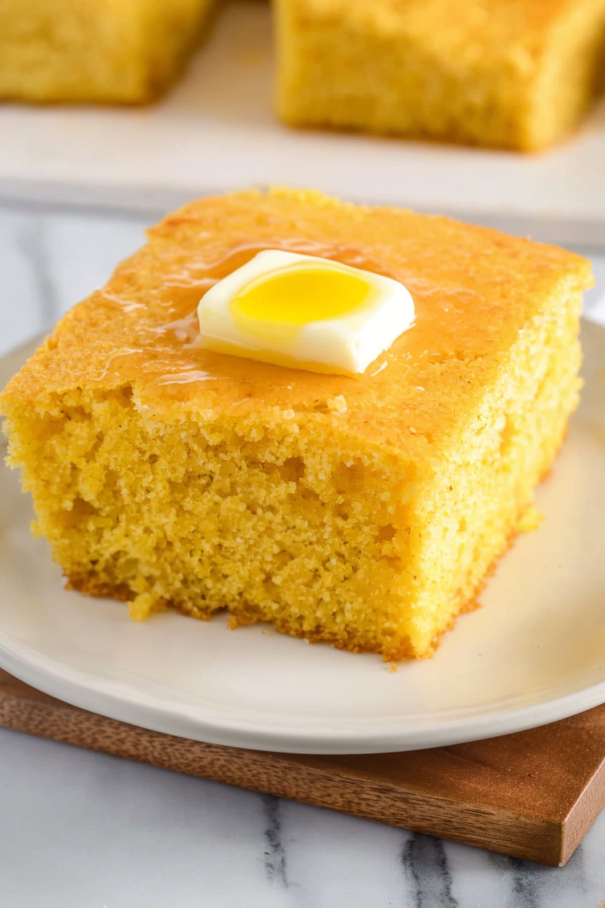 A slice of golden cornbread on a plate topped with a melting pat of butter.