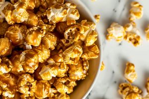 Microwave Caramel Popcorn in a Bowl on a White Marble Table with More Popcorn on the Table