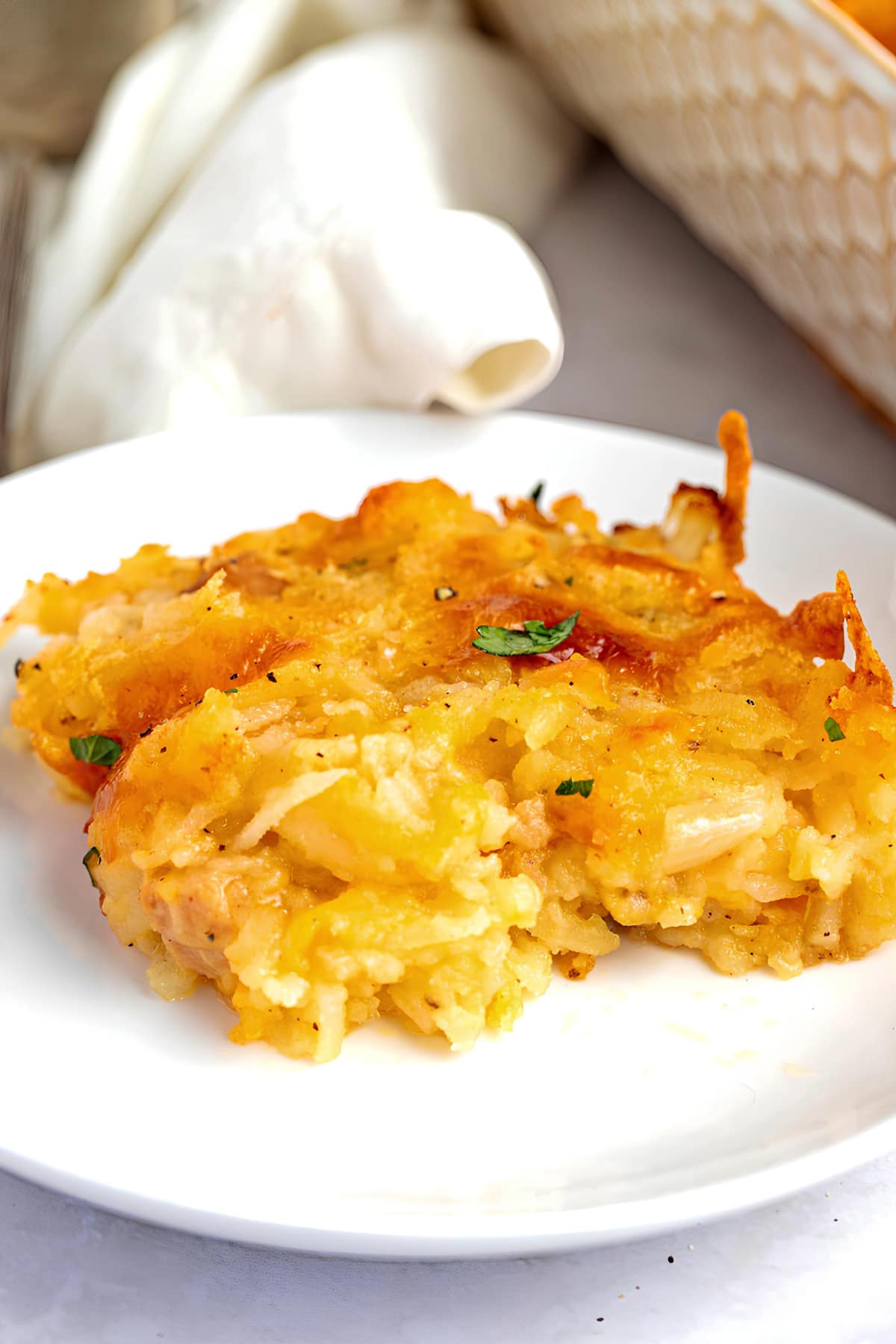 A serving of cheesy Hash brown casserole on a white saucer.