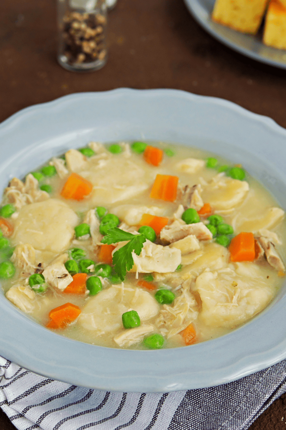 Bowl of soup with chicken, dumplings, carrots and chopped onion leaves.