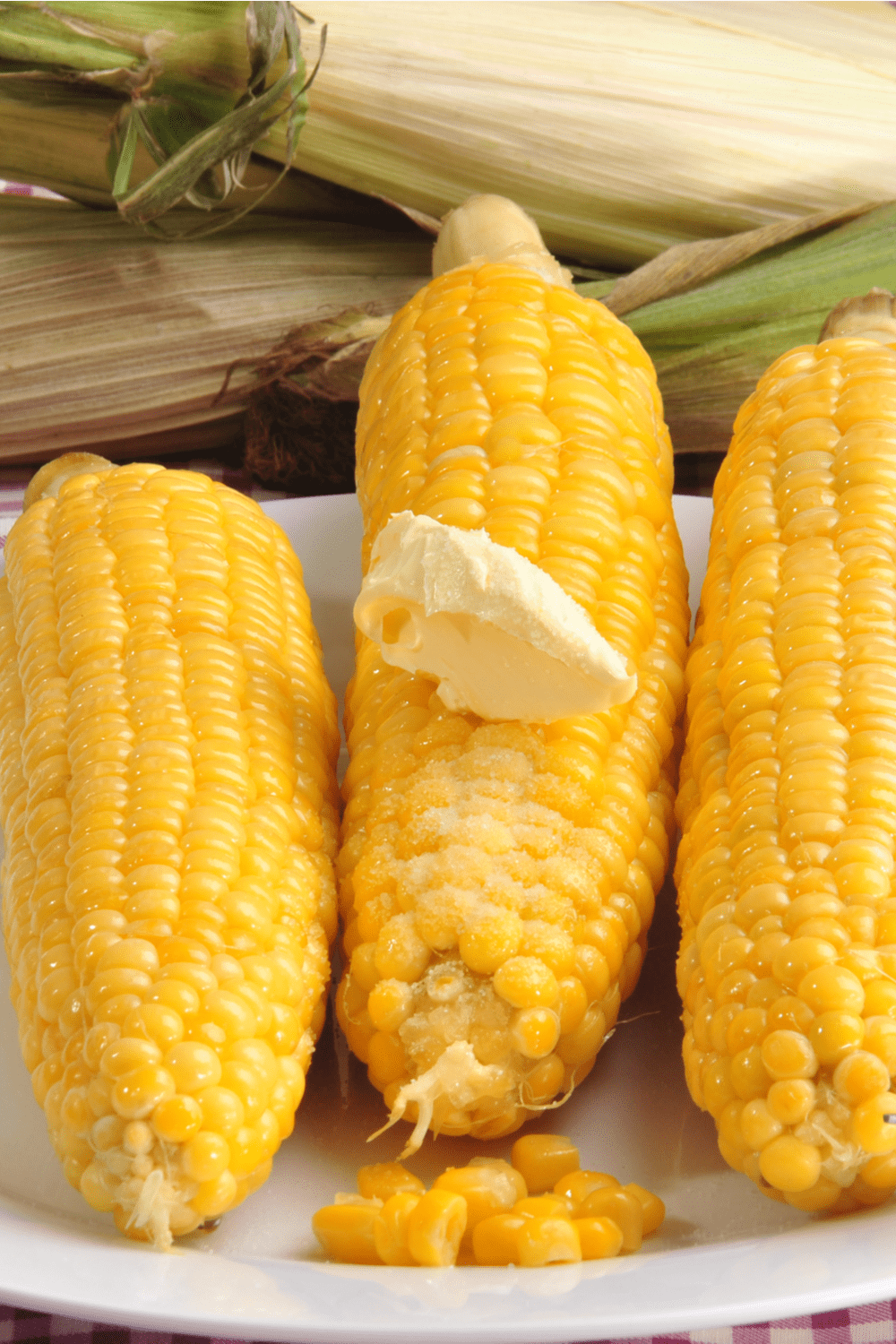 Three cooked yellow corn with a piece of butter served on white plate. 