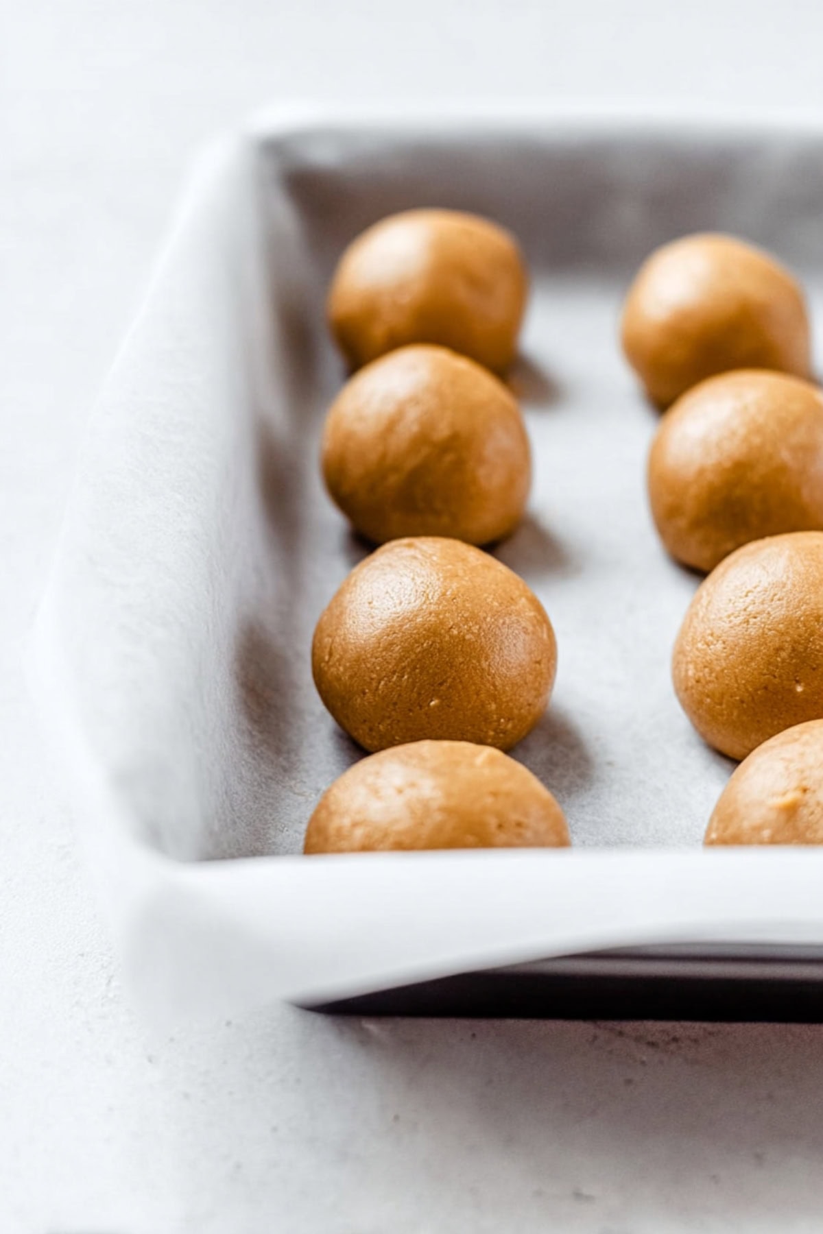 Peanut butter dough balls in a baking pan on a parchment paper.