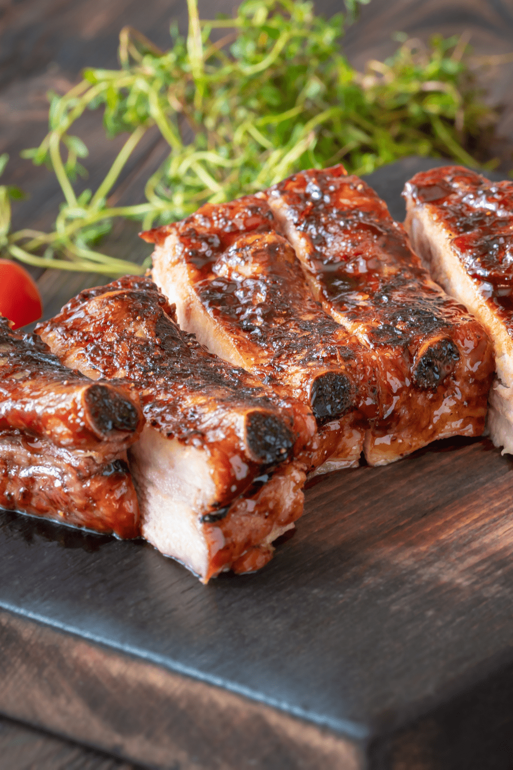 Bone-In Air Fryer Barbecue-Glazed Pork Ribs with Sauce on a Cutting Board with Herbs in the Background