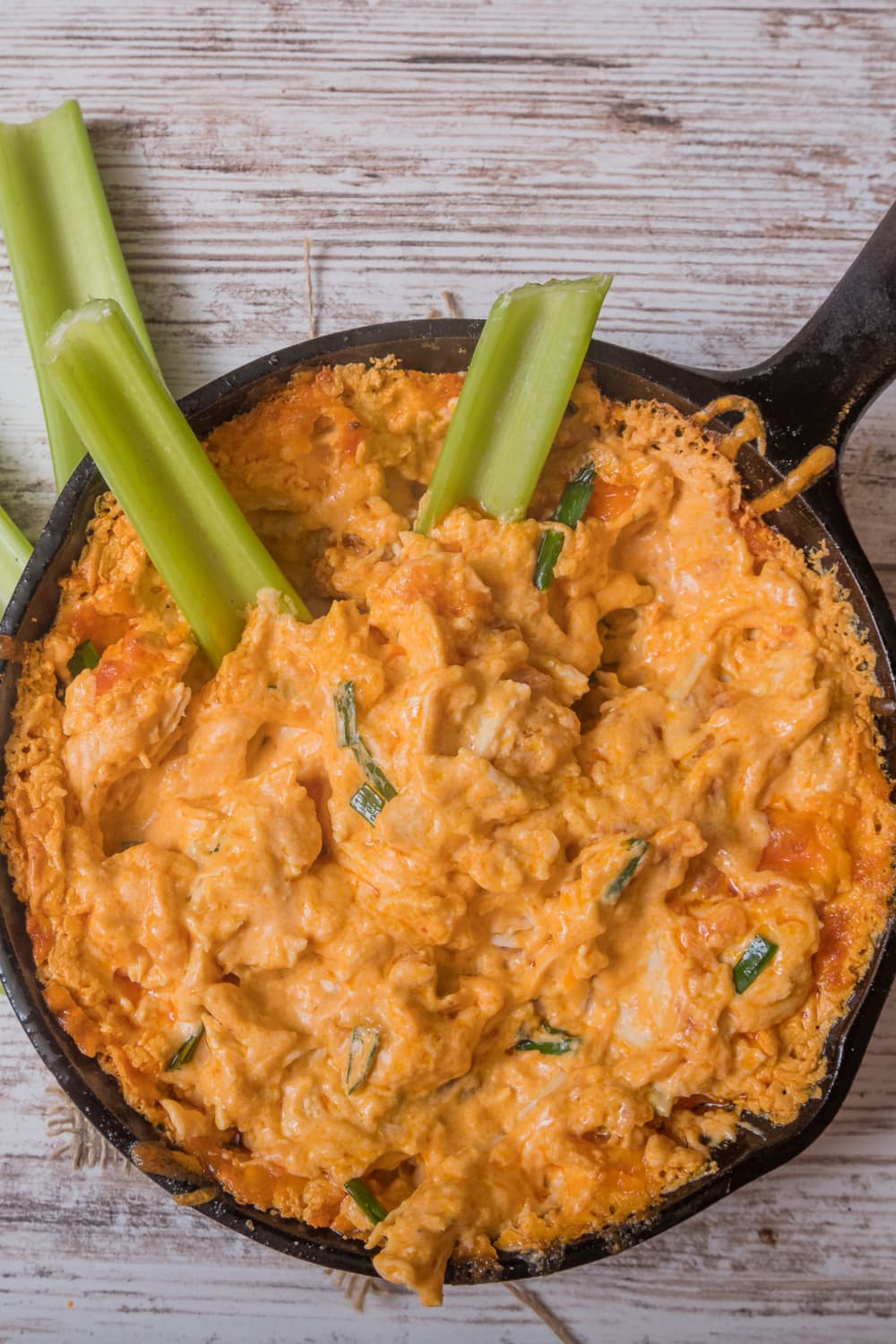 Buffalo Chicken Dip cooked in a cast iron pan with fresh celery stalks dipped on it. 