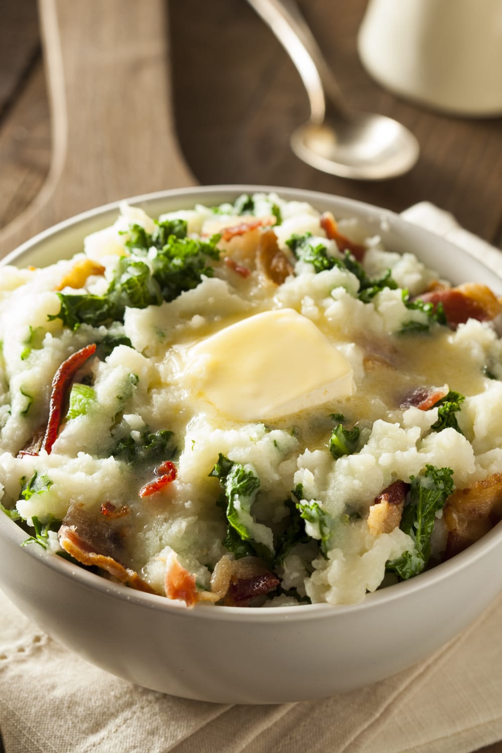 A bowl of Mashed Potatoes with mashed potatoes mixed with cabbage, greens and bacon topped with melted butter.