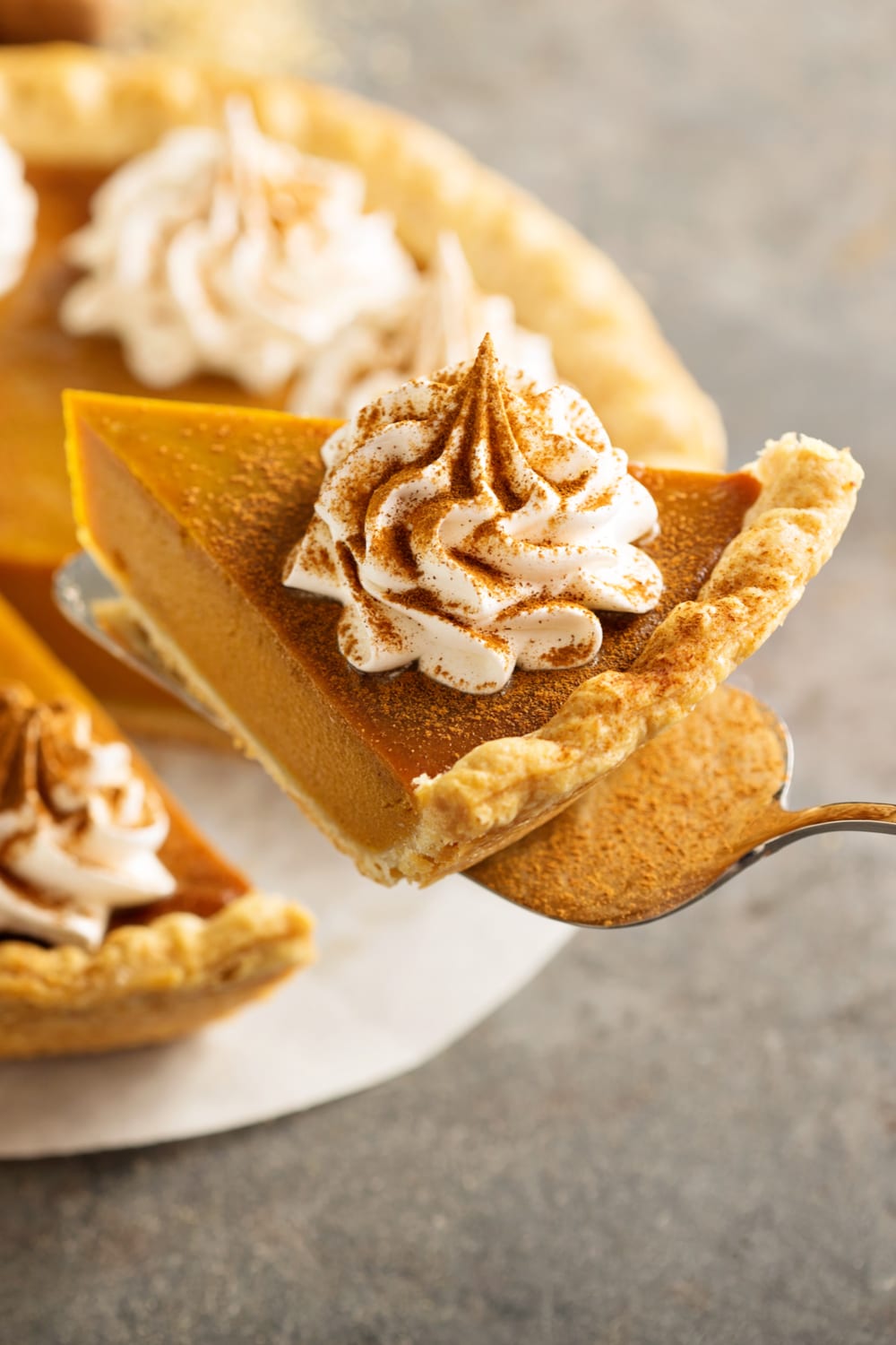 A slice of pumpkin pie topped with a pump of cream picked with a pie server. 