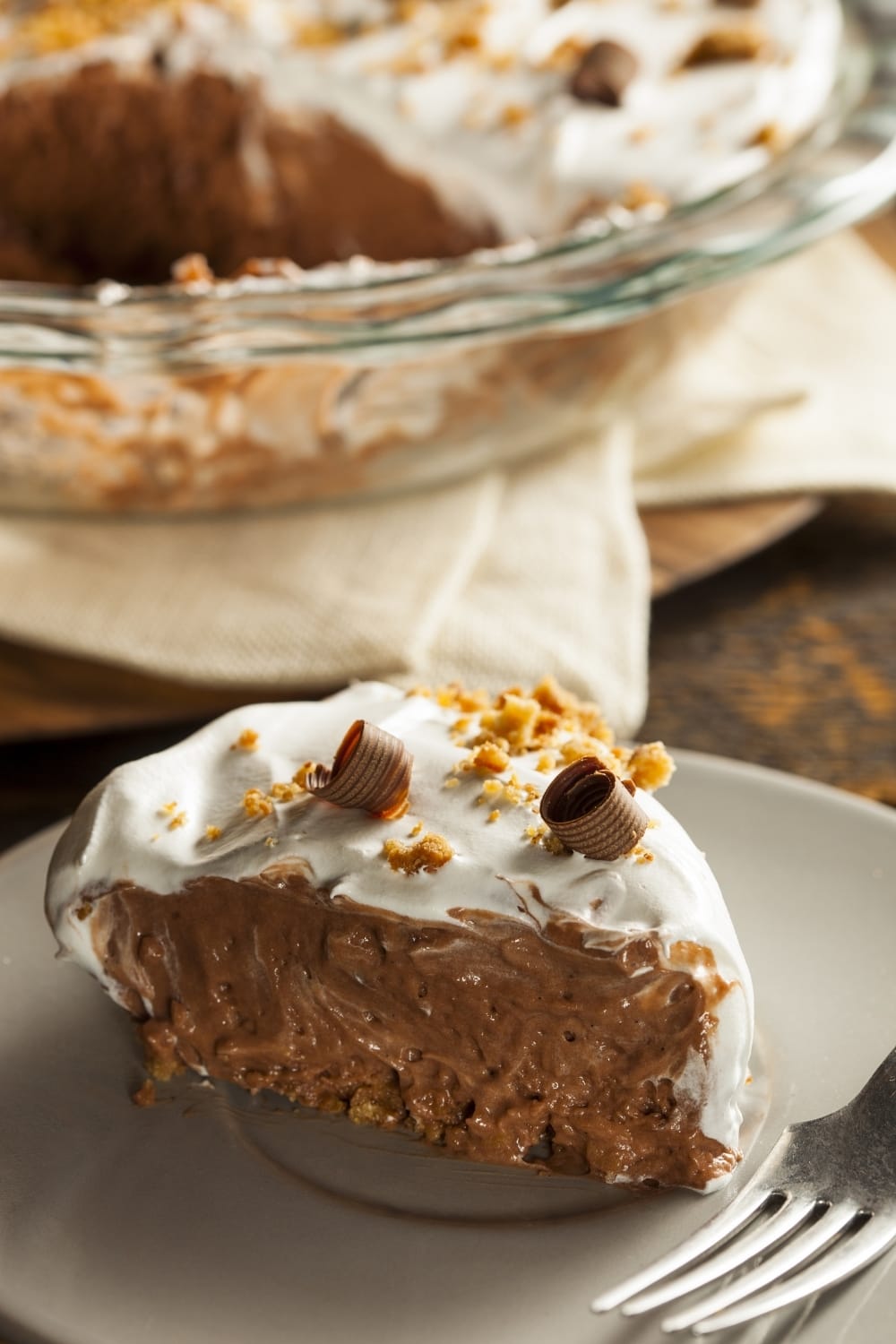 A slice of chocolate pie with whipped cream cover topped with chopped nuts and chocolate shavings. 